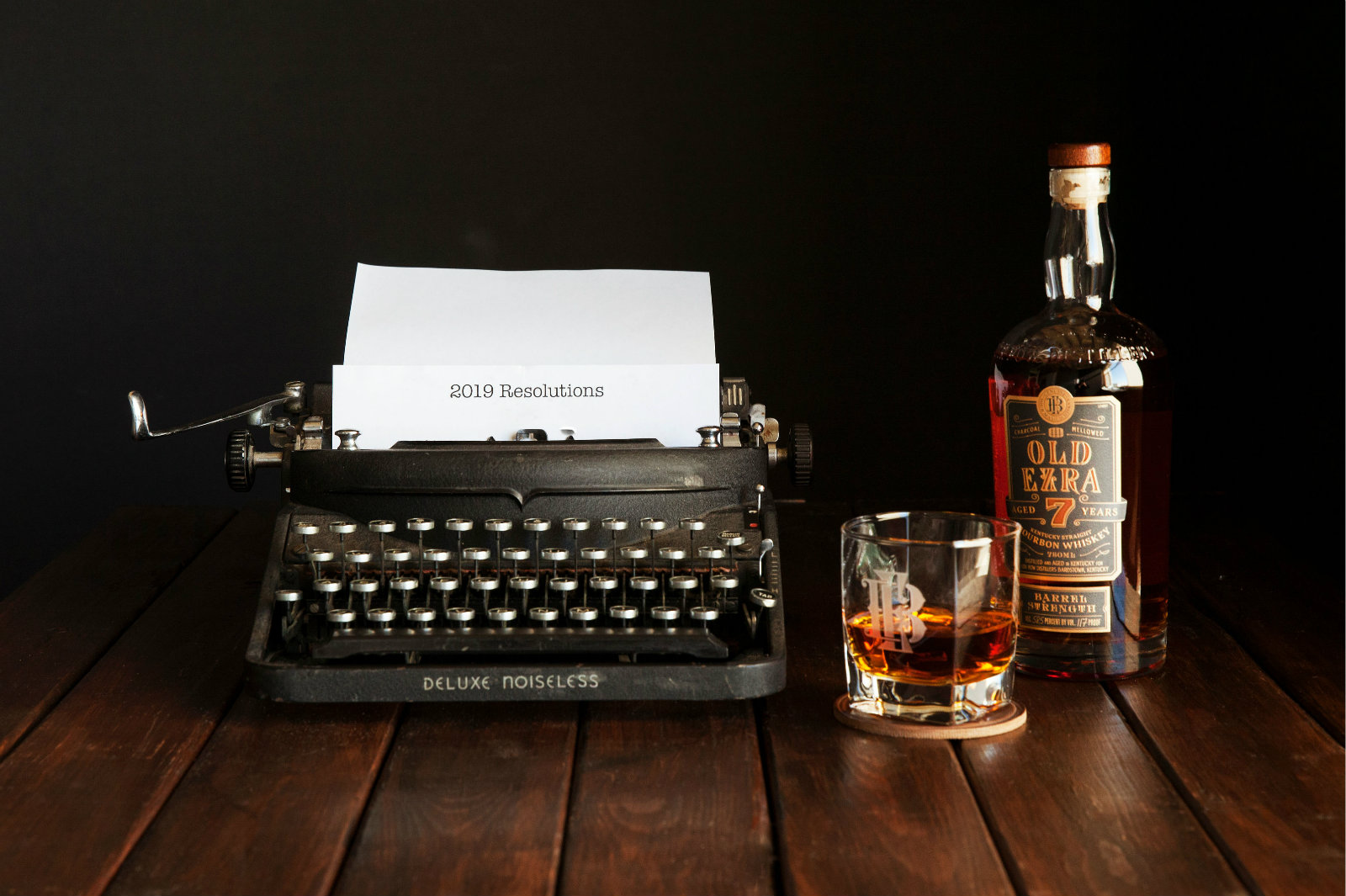 A bottle of Old Ezra and a glass of bourbon sitting next to a typewriter